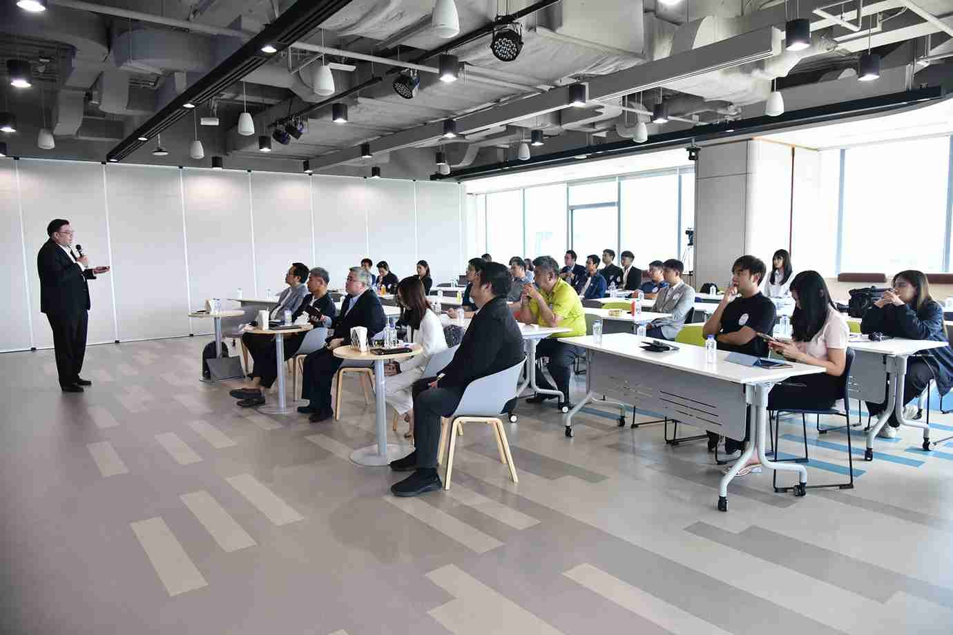 Speaker addresses attendees seated at tables in a bright, modern conference room.