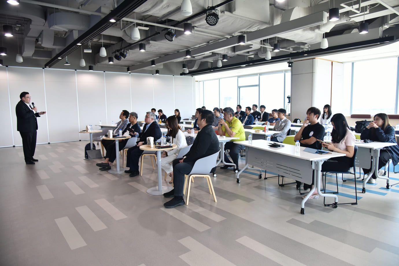 Speaker addresses an audience at a business conference in a modern, well-lit room.