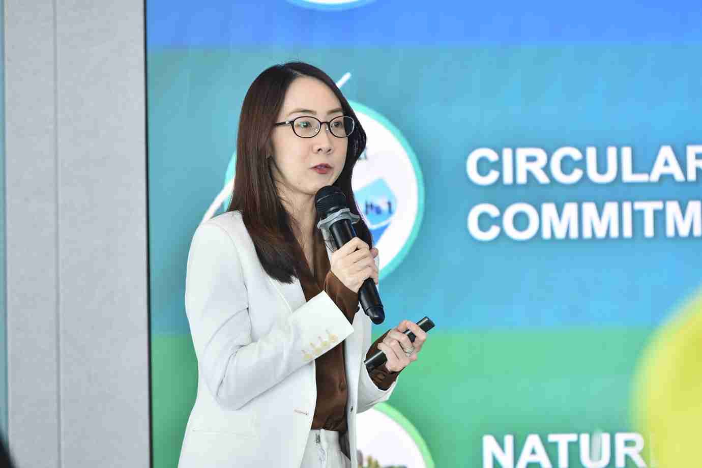 Woman in white blazer and glasses speaks into a microphone during a presentation.
