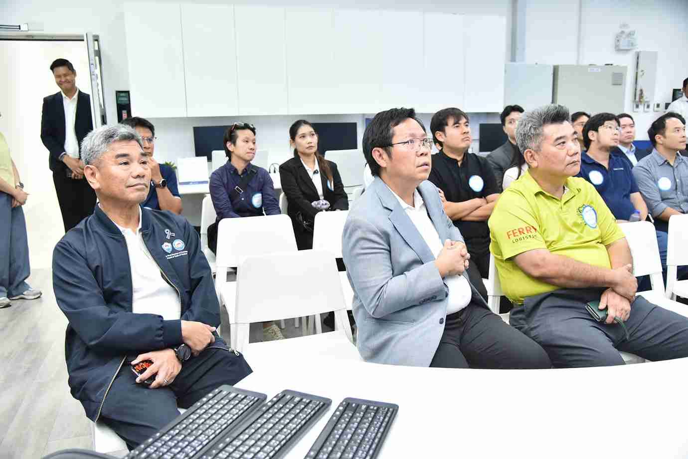 Group of attentive people sitting in a classroom-like setting, watching a presentation.