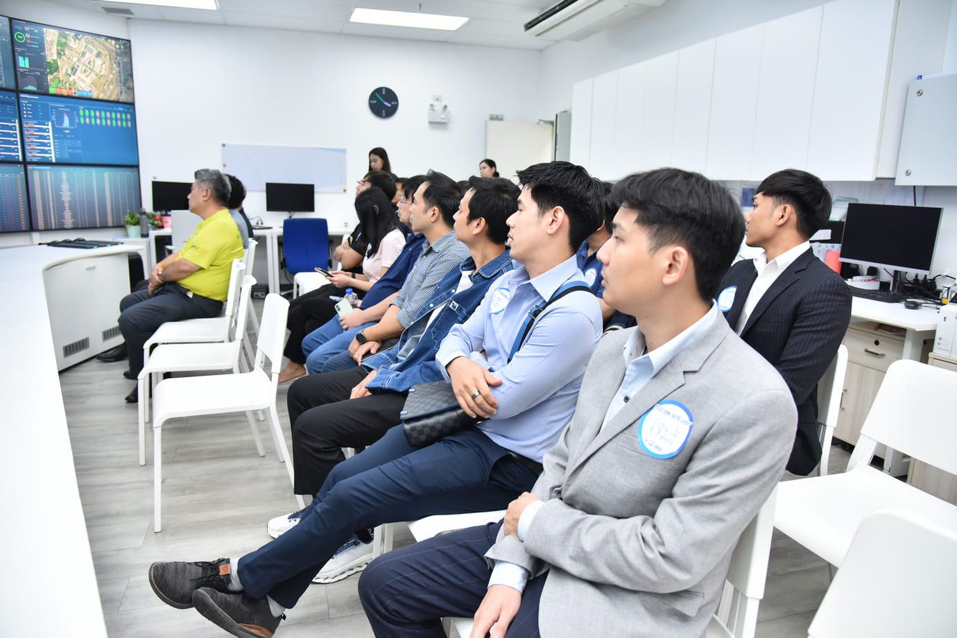 Attendees watch multi-screen data displays in a modern control room or training facility.