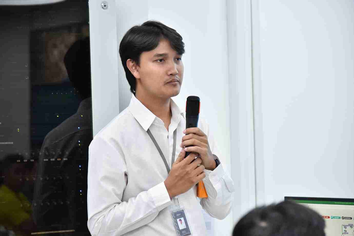 Young man in white shirt speaking into a microphone during a presentation.