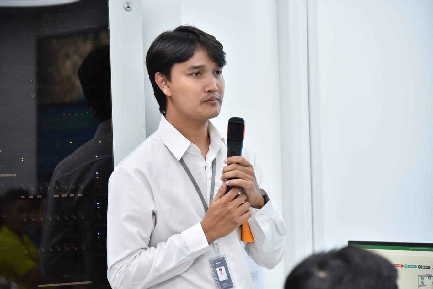 Young man in white shirt speaking into a microphone at an event.