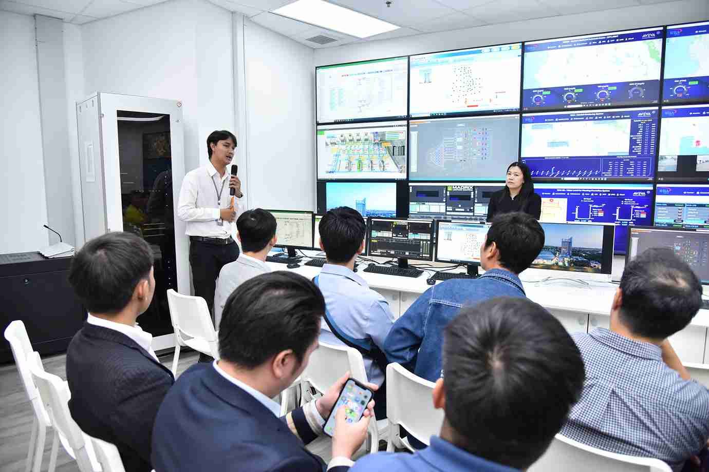 Man presents to professionals in a control room with multiple data monitors.