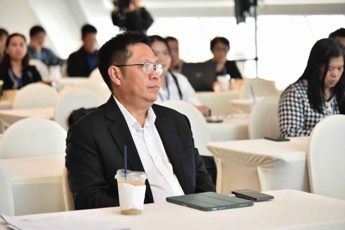 A man in glasses and a suit listens attentively at a conference table.