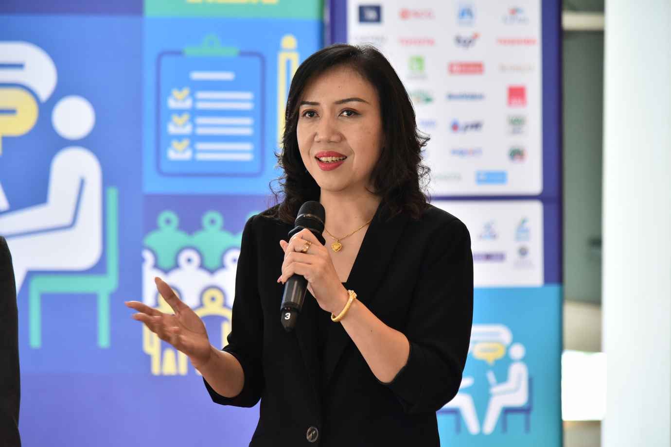 Woman in black blazer speaks into microphone at a professional presentation.