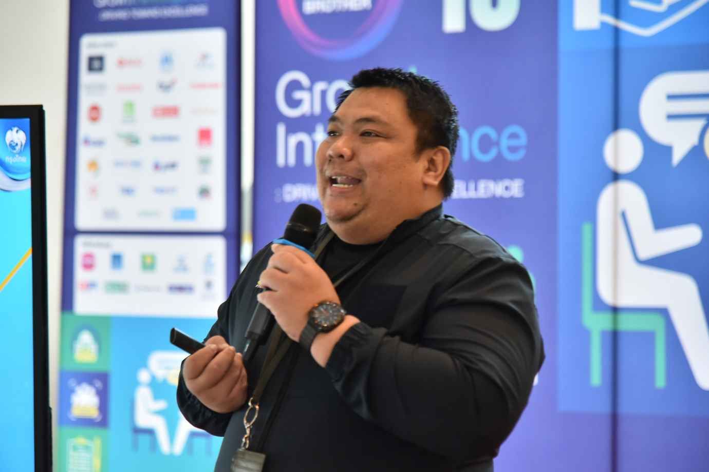 A man in a black shirt speaks into a microphone at a professional event.