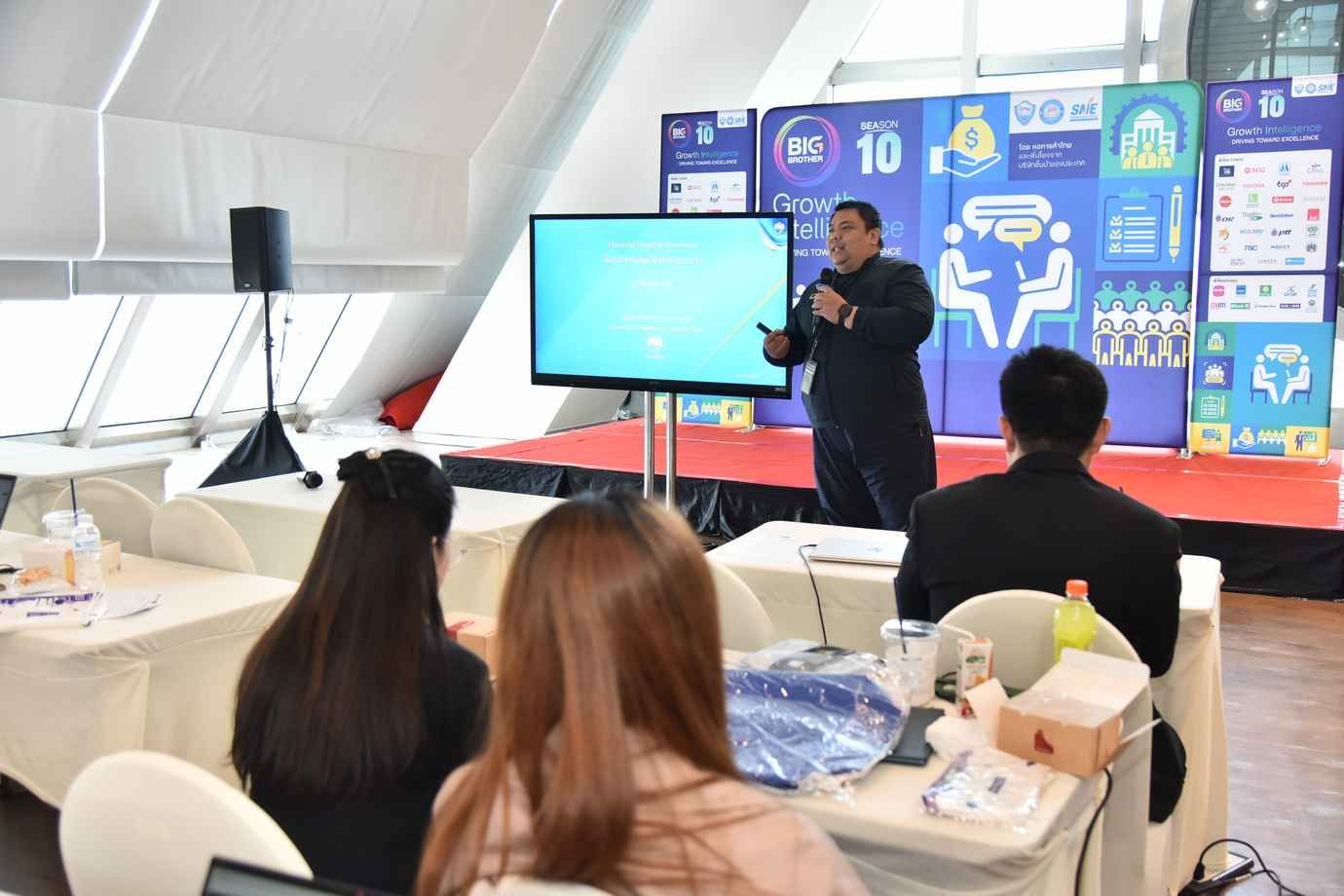 A speaker presents information on a screen to an audience at a professional event.