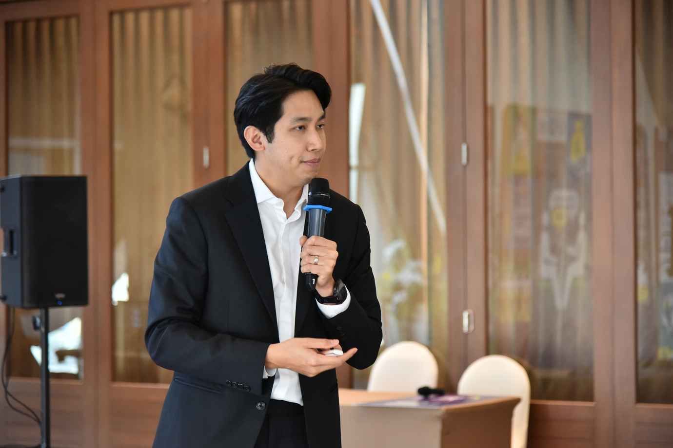 Man in black suit speaking into a microphone during a presentation.
