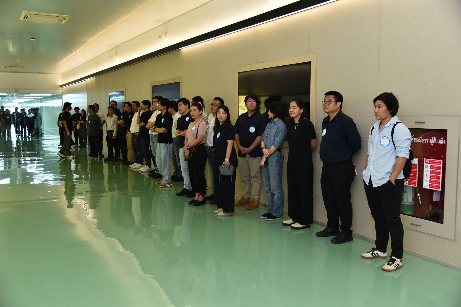 A group of diverse professionals stands in a modern, brightly lit corridor, lining a wall.