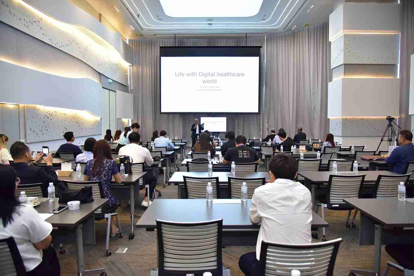 Attendees at a professional conference listen to a speaker in a modern meeting room.
