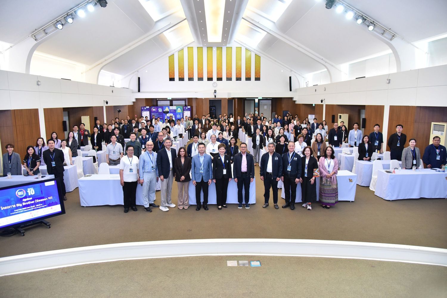 A large group of people, many in business attire, stand together in a spacious conference hall.