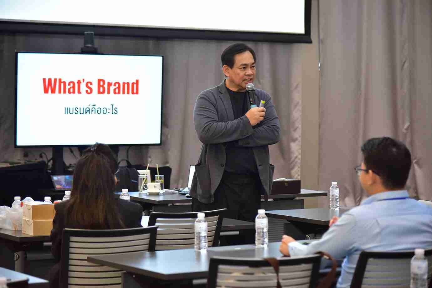 Man presenting 'What's Brand' on a screen to an audience in a seminar room.