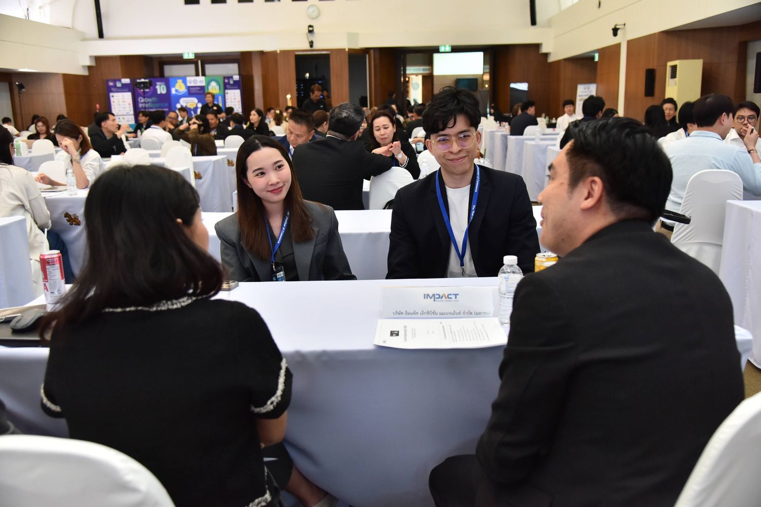 Two women and a man listen attentively to another man at a rectangular table during an event.