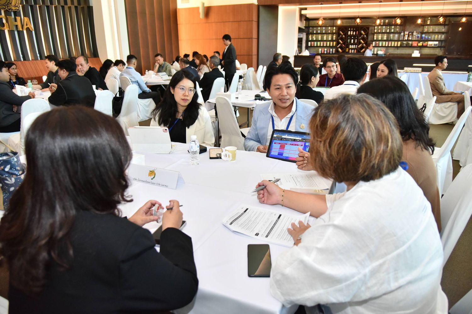 Four attendees sit at a round table, two looking at a tablet during a conference.