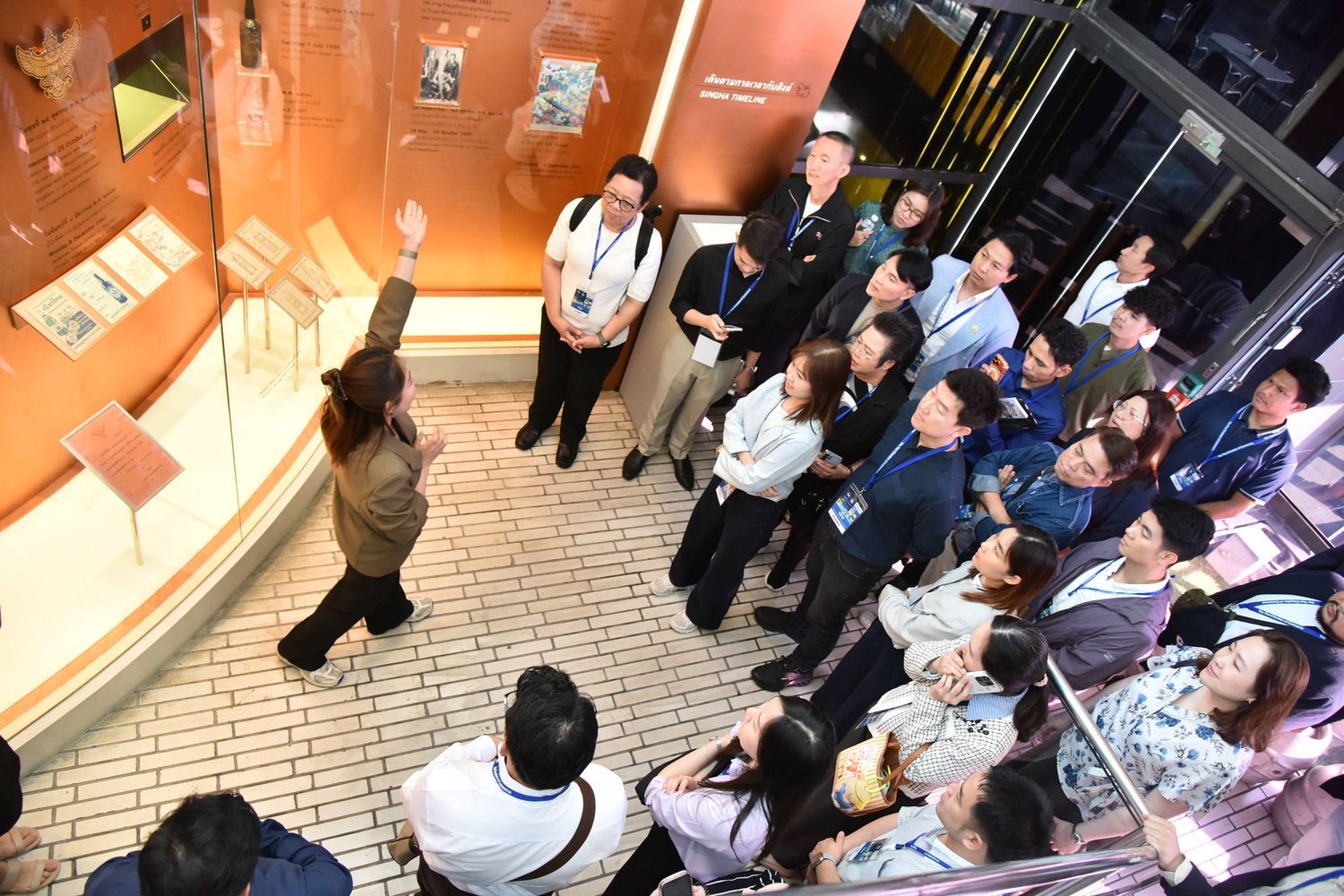 A speaker addresses an engaged audience in a modern exhibition space with various displays.