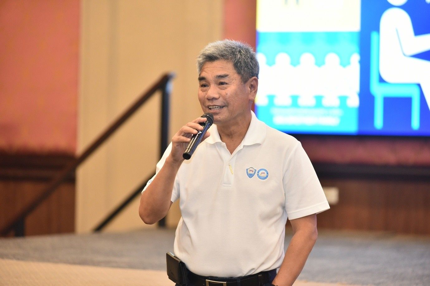 Middle-aged Asian man speaking into a microphone at an indoor event.