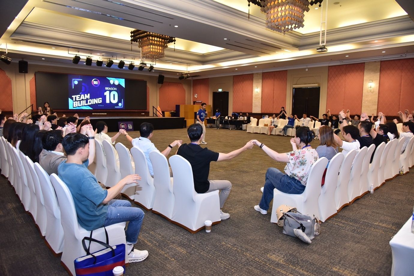 People holding hands in an event hall during a team building activity.