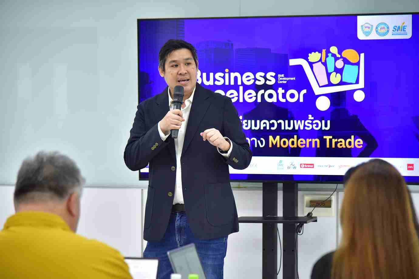 Man speaks into microphone at a Business Accelerator event in front of a large screen.