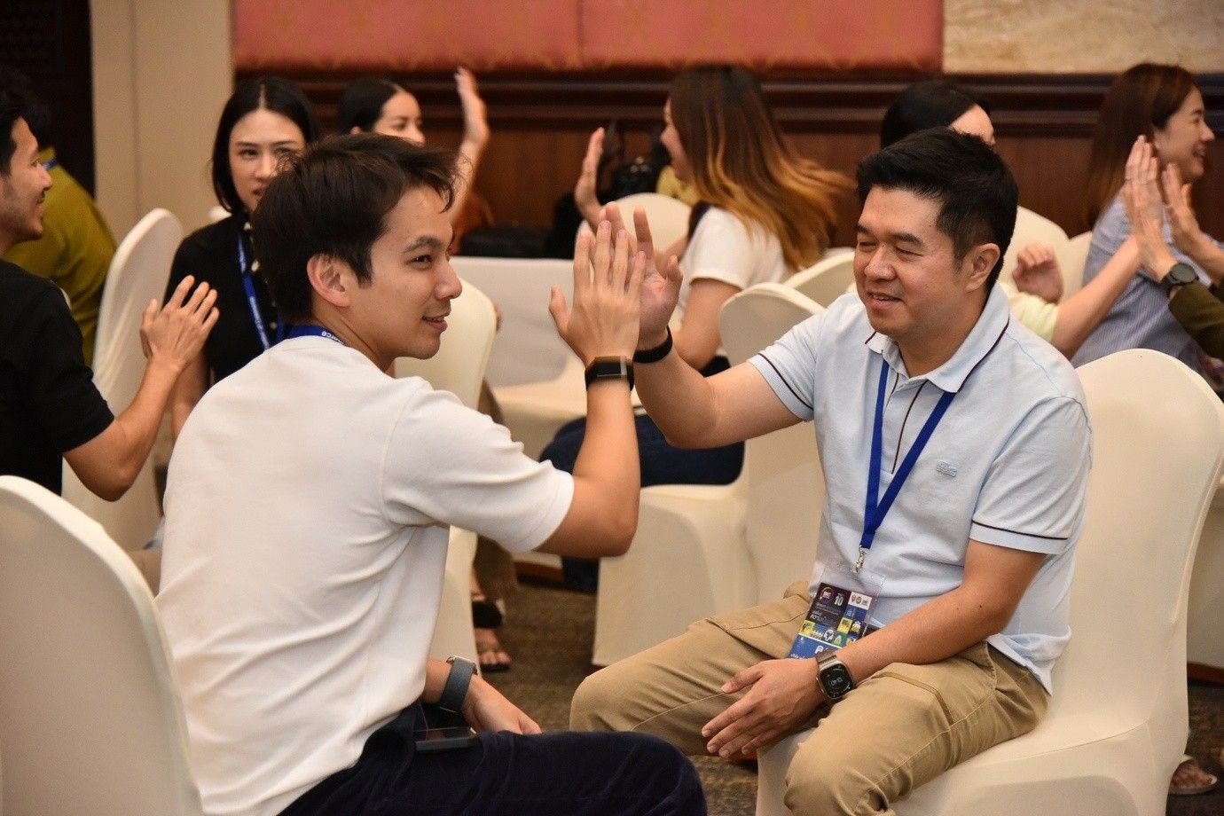 Two men high-fiving while sitting in chairs at an indoor event.