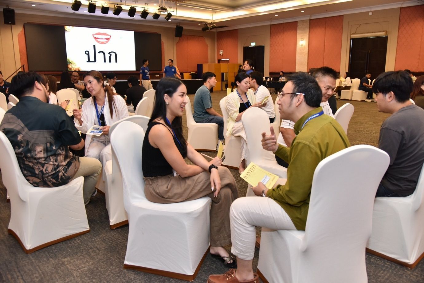 Attendees sit in white chairs, discussing in small groups at a conference event.