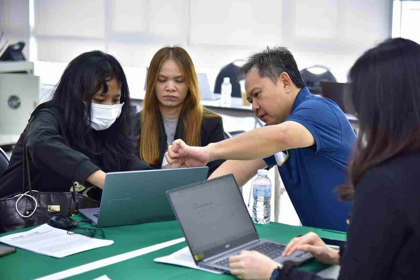 Four professionals collaborate intently around laptops at a meeting table.