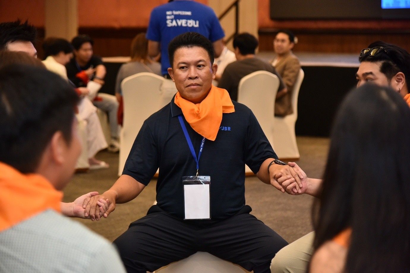 Man in orange scarf leads group activity, holding hands in a circle.