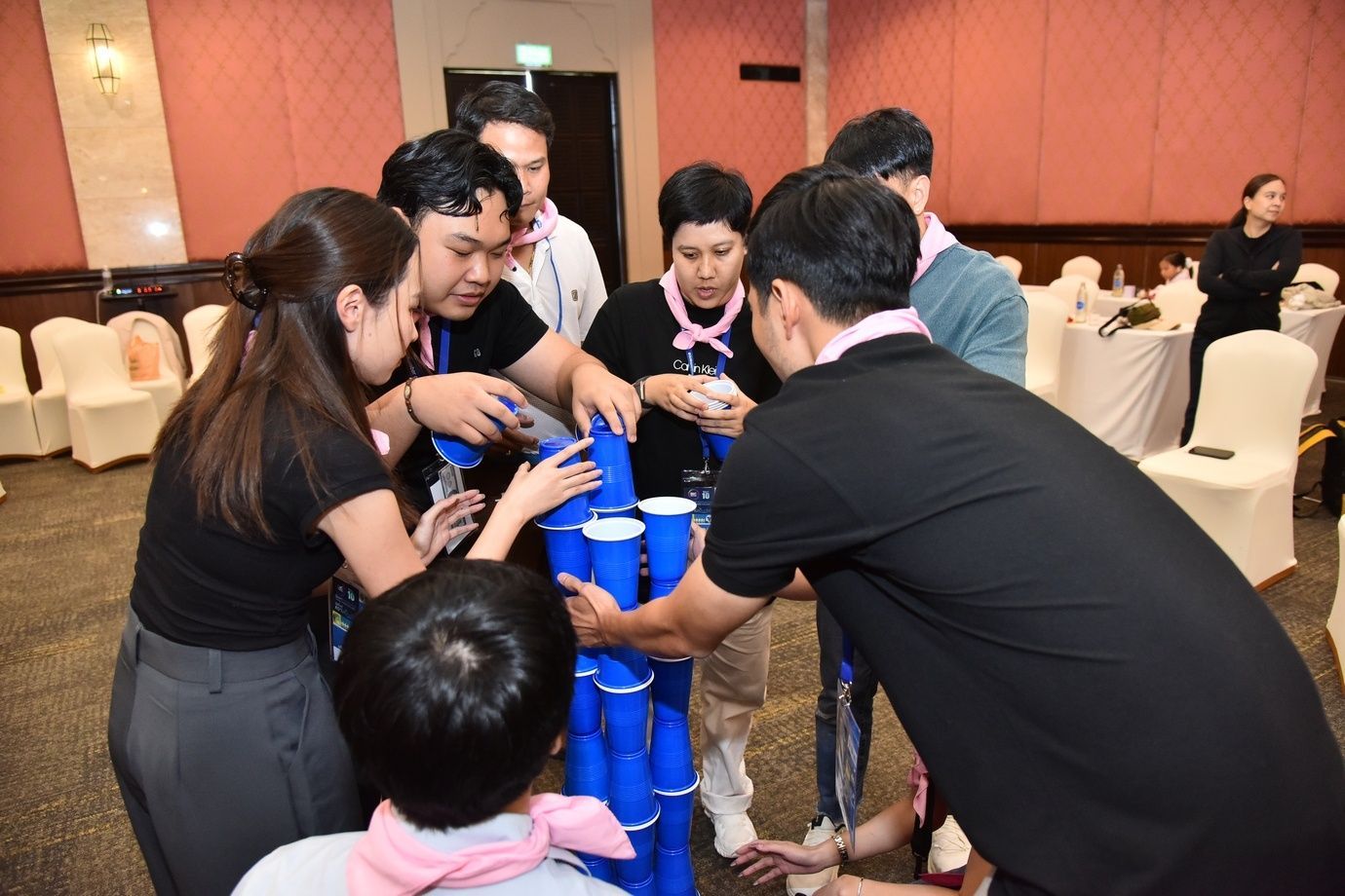A group of people collaboratively building a tall structure using blue plastic cups.