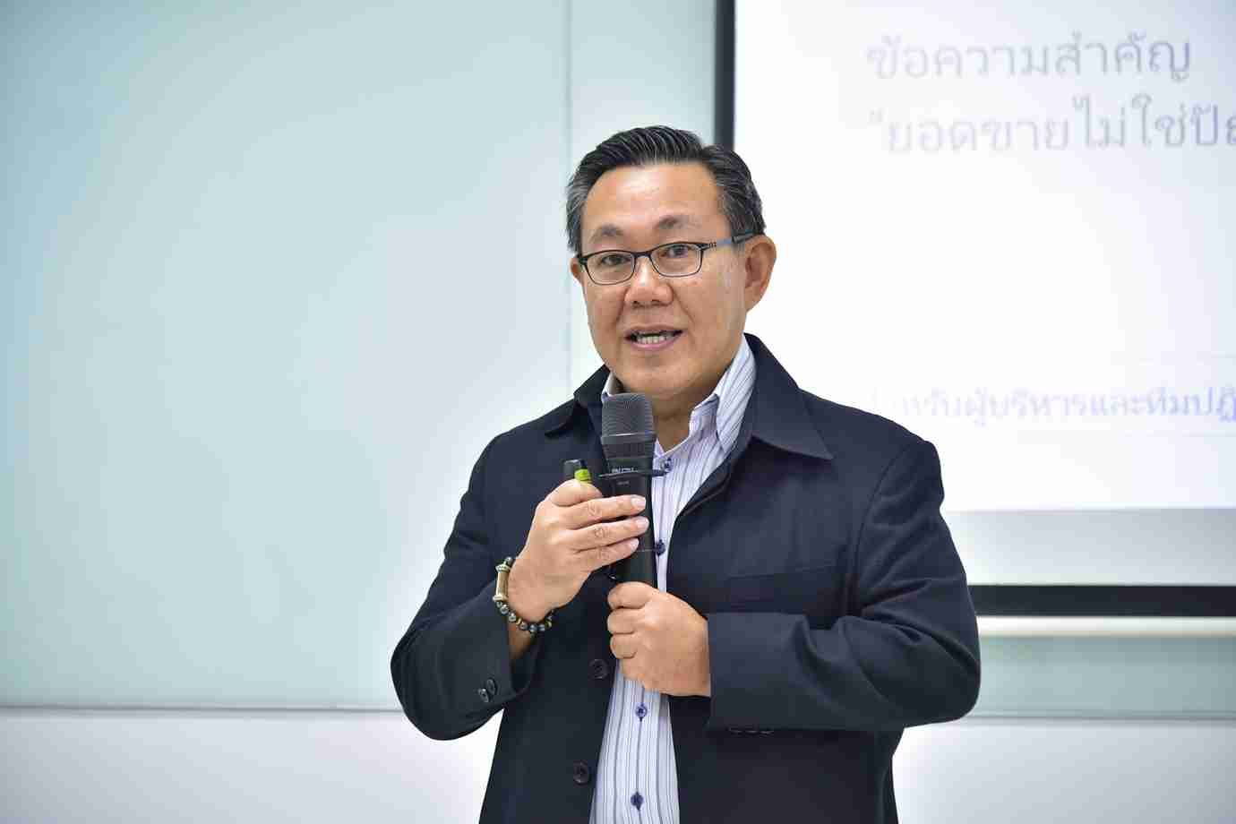 Man in glasses and a dark jacket speaks into a microphone during a presentation.