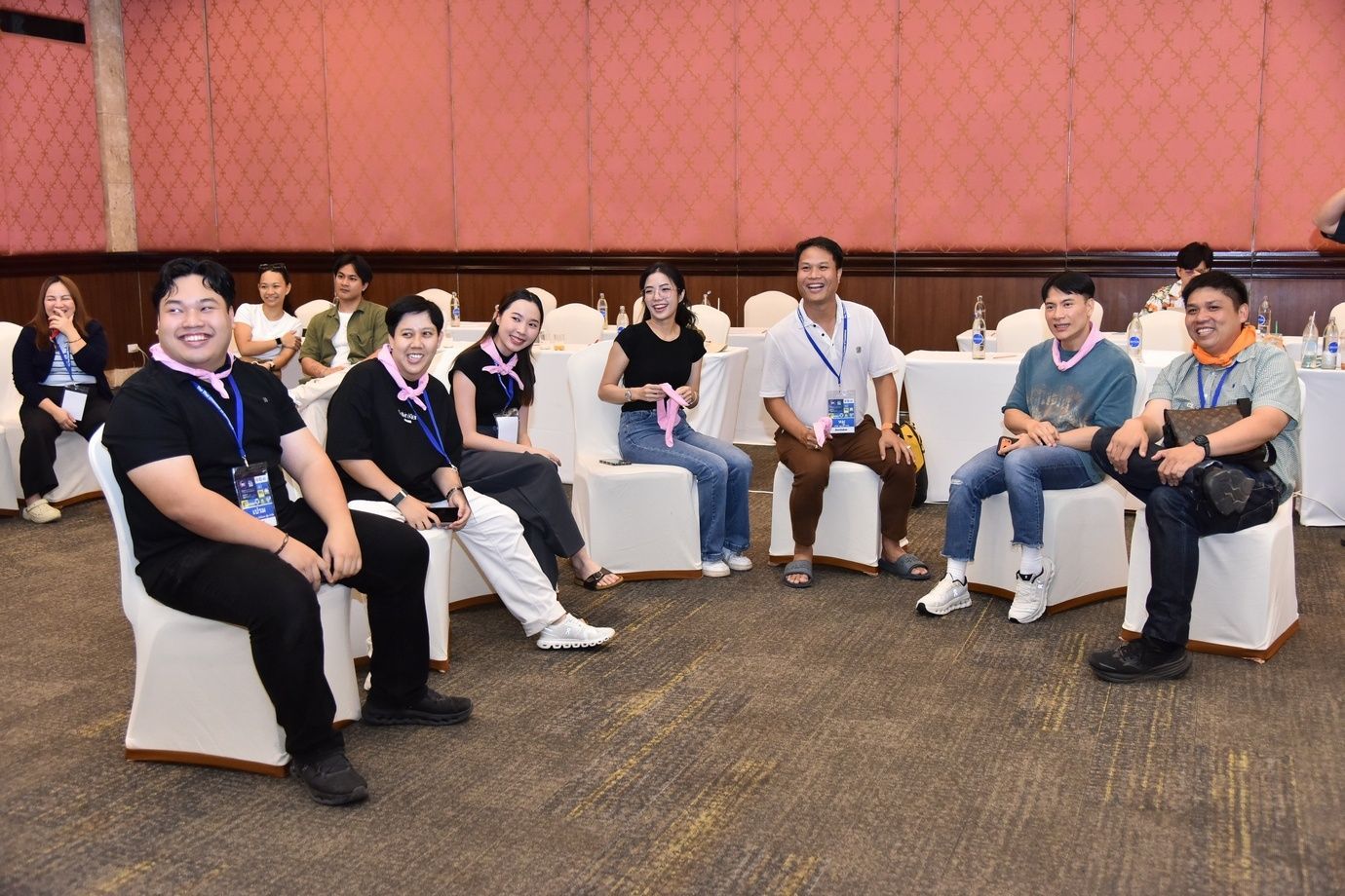 A group of smiling individuals sits in a semi-circle within a conference room.