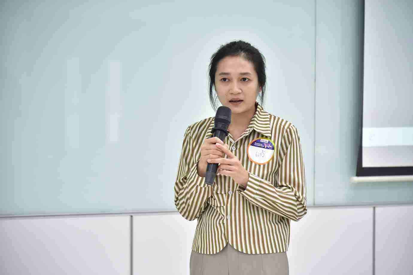 Woman in striped shirt speaking into a microphone during a presentation.