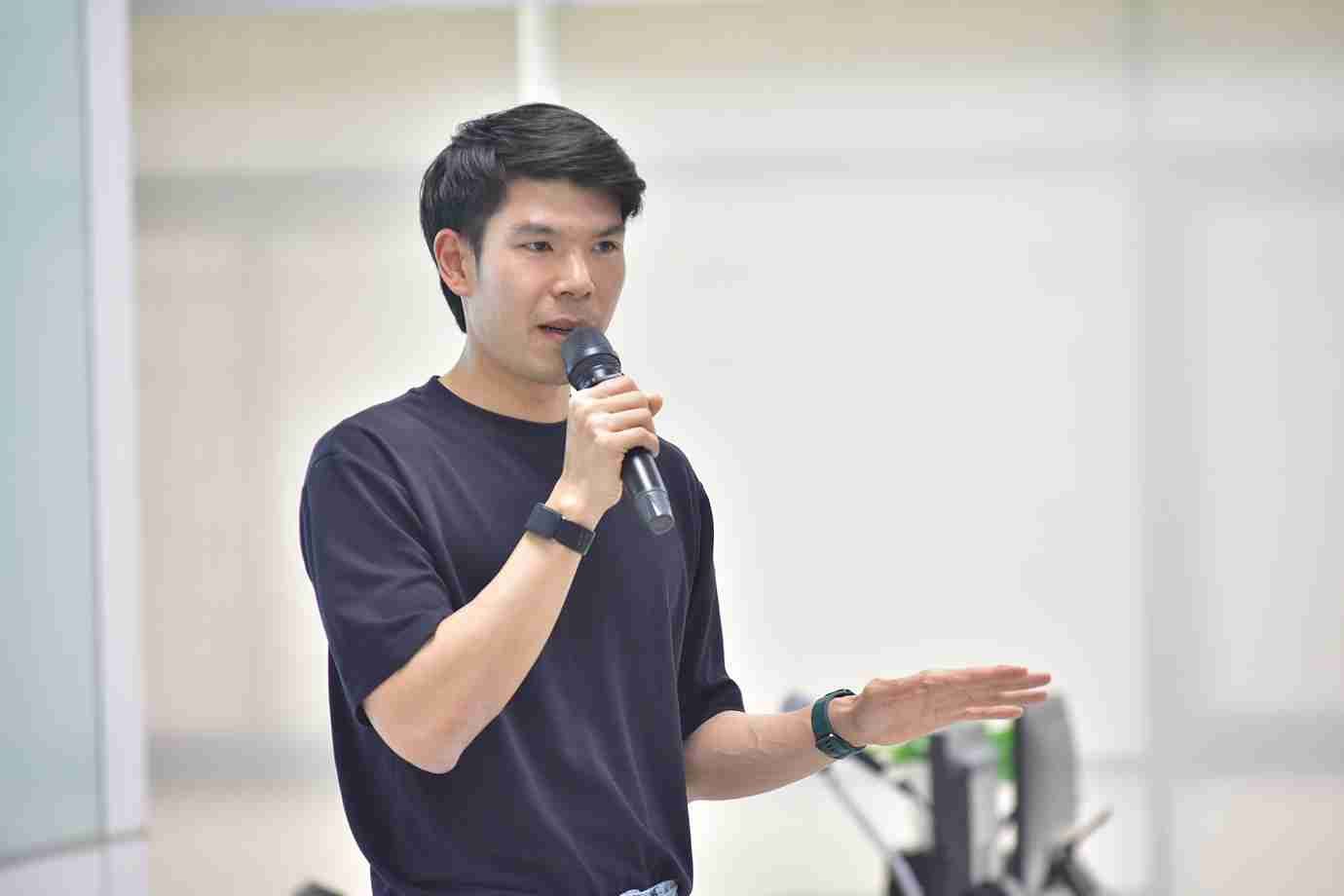 Man speaking into a microphone with his right hand gesturing during a presentation.