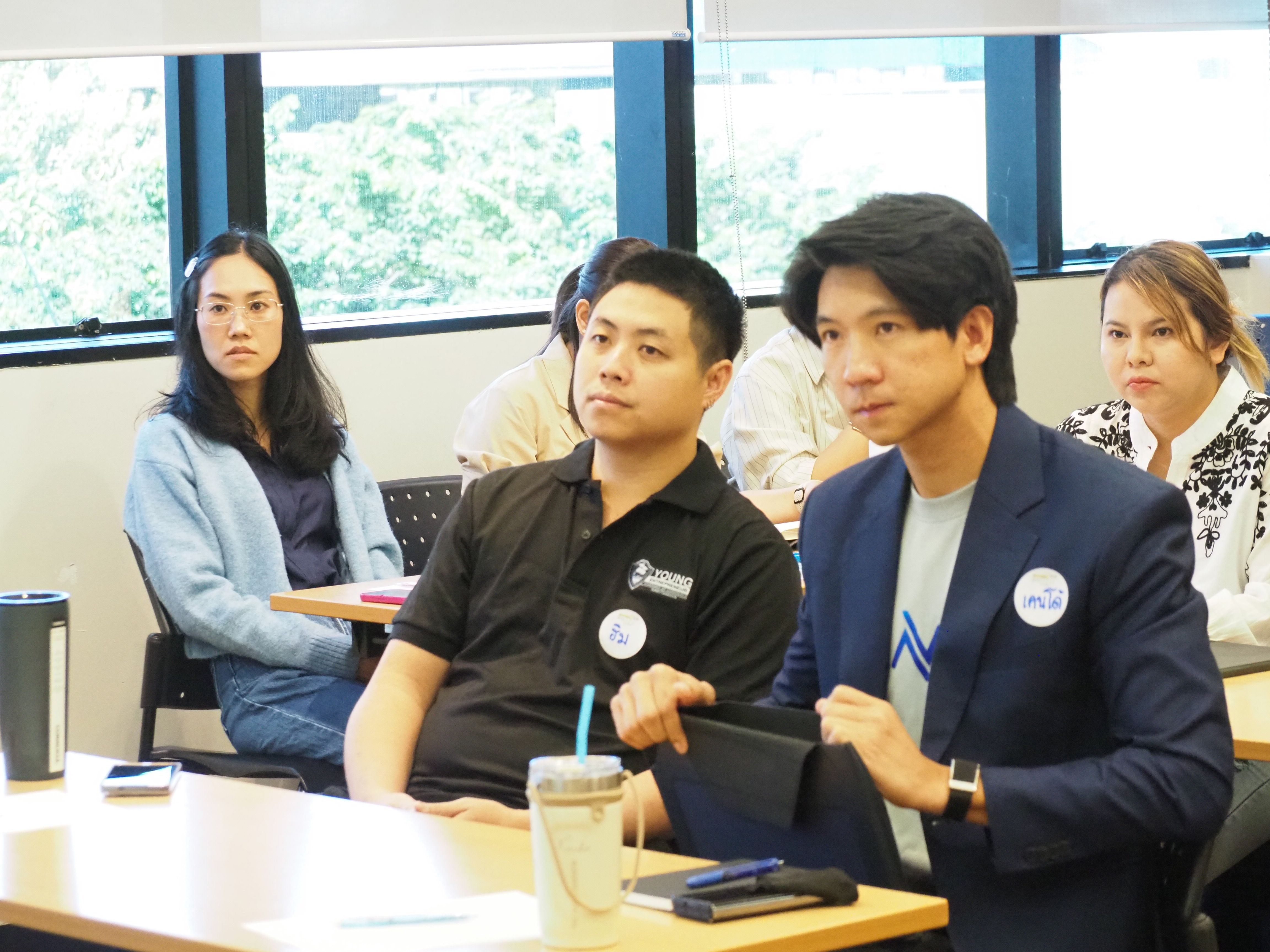 Two men and a woman attentively listen in a bright classroom setting.