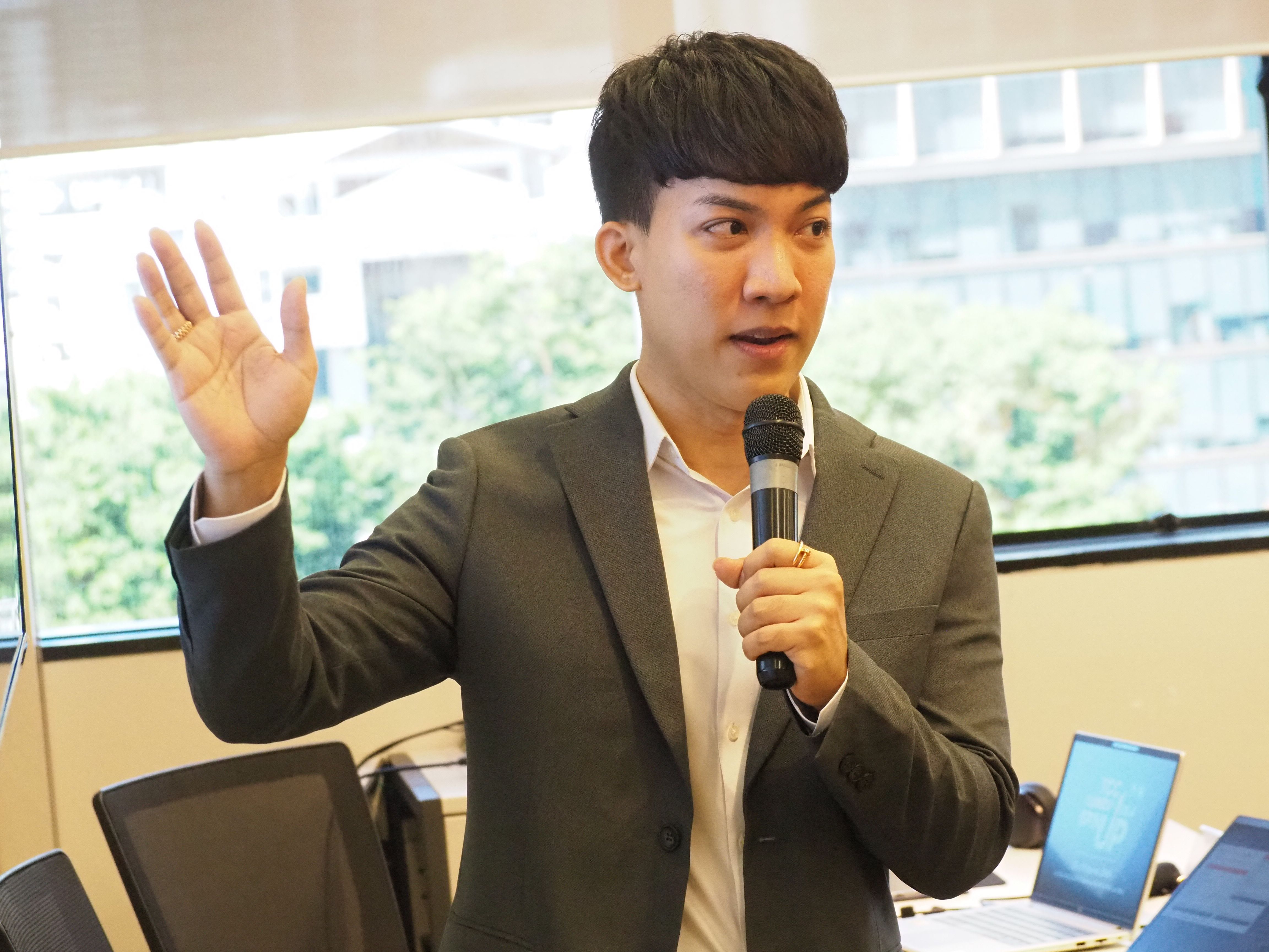 Man speaking into a microphone with hand raised during a presentation.