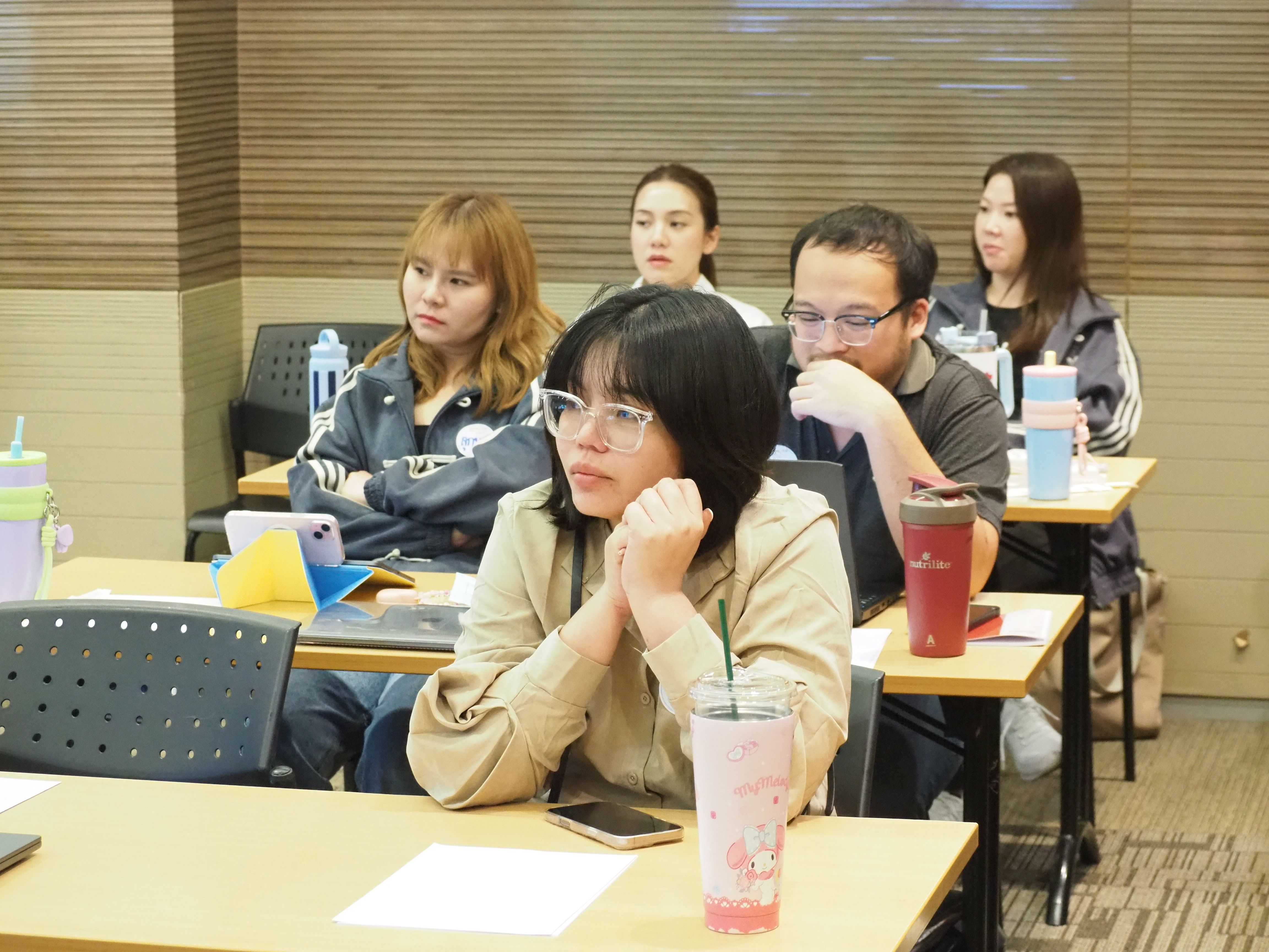 Young woman in glasses listening intently in a classroom setting with others.