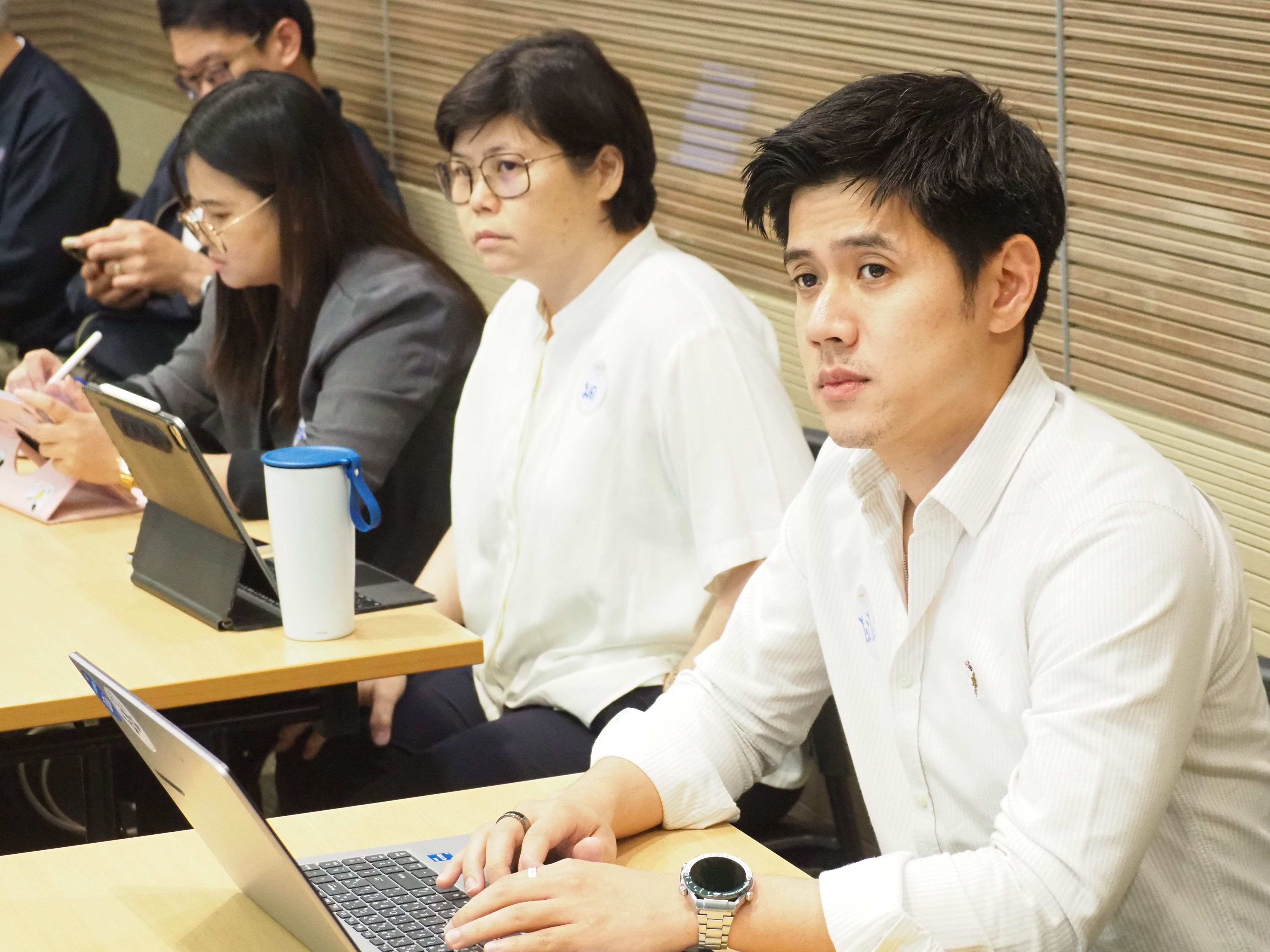 Young man in white shirt focused on a laptop during a professional meeting with colleagues.