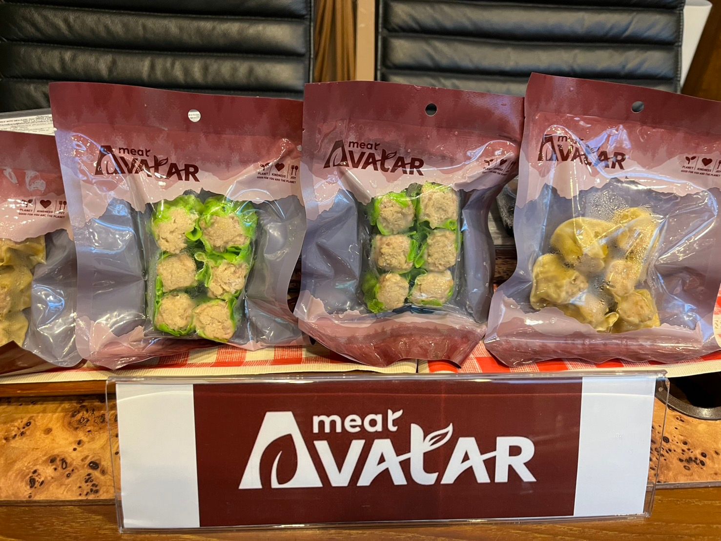 Three packages of 'meat AVATAR' plant-based dumplings, two green and one yellow, on a display.