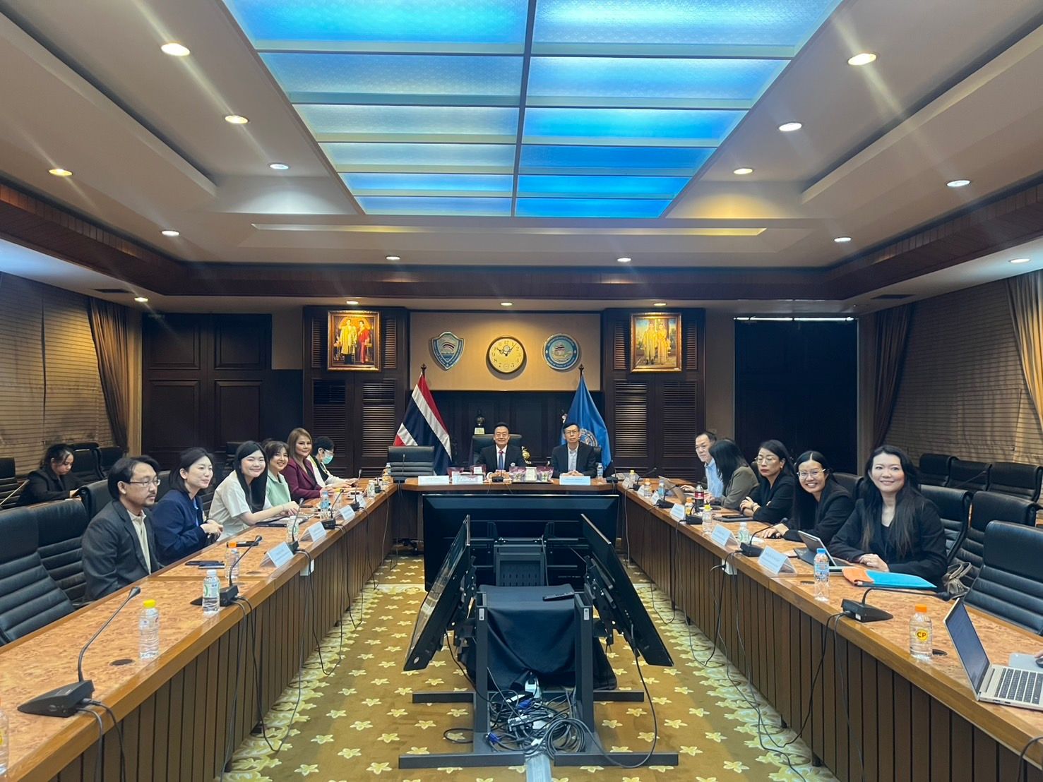Professionals attend a formal meeting in a spacious conference room with a flag visible.