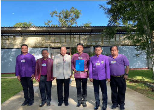 Six men in official attire stand outdoors, one holding a blue document.