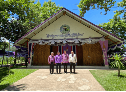 Four men in traditional shirts stand in front of a decorated Thai building.