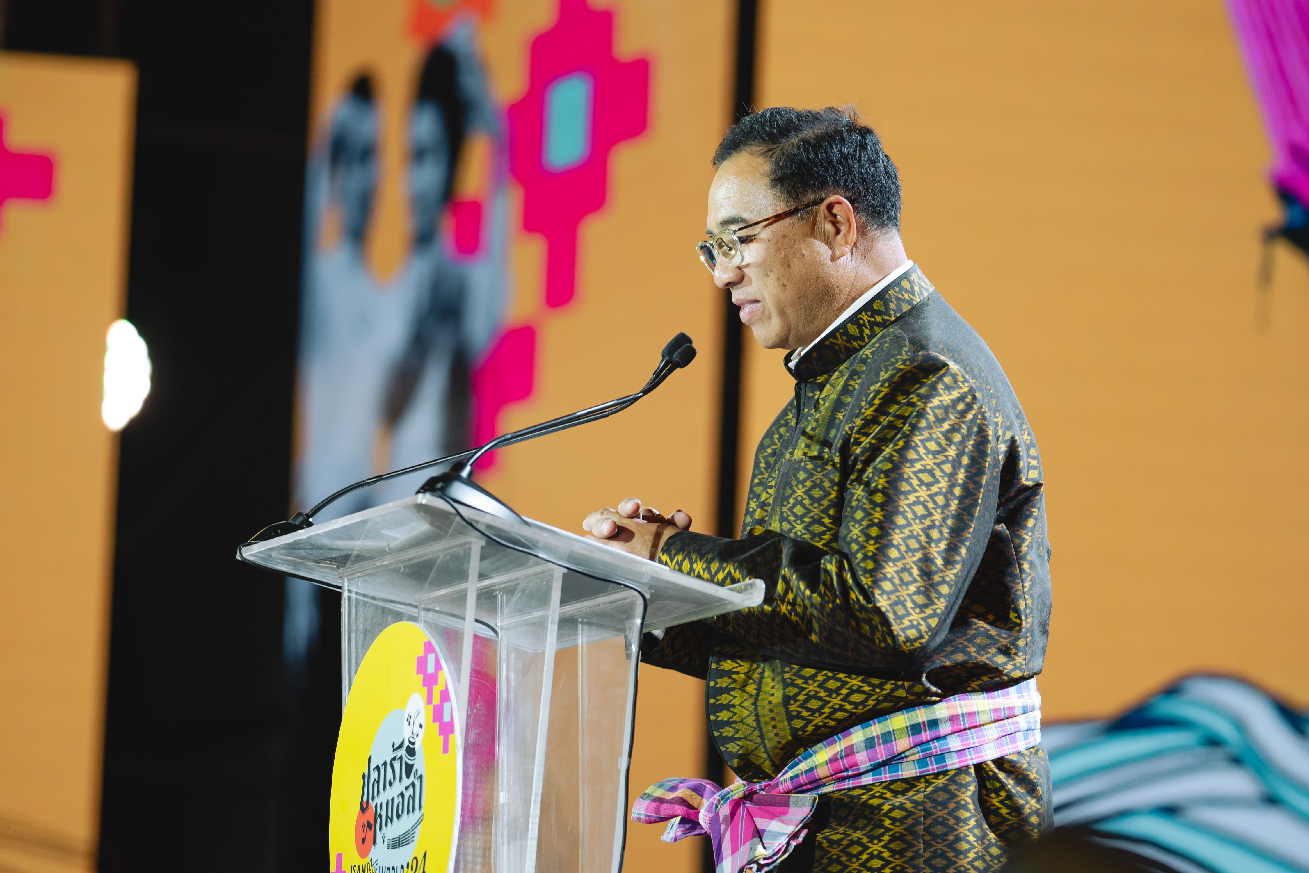 Man in traditional patterned shirt speaks at a podium with a microphone.