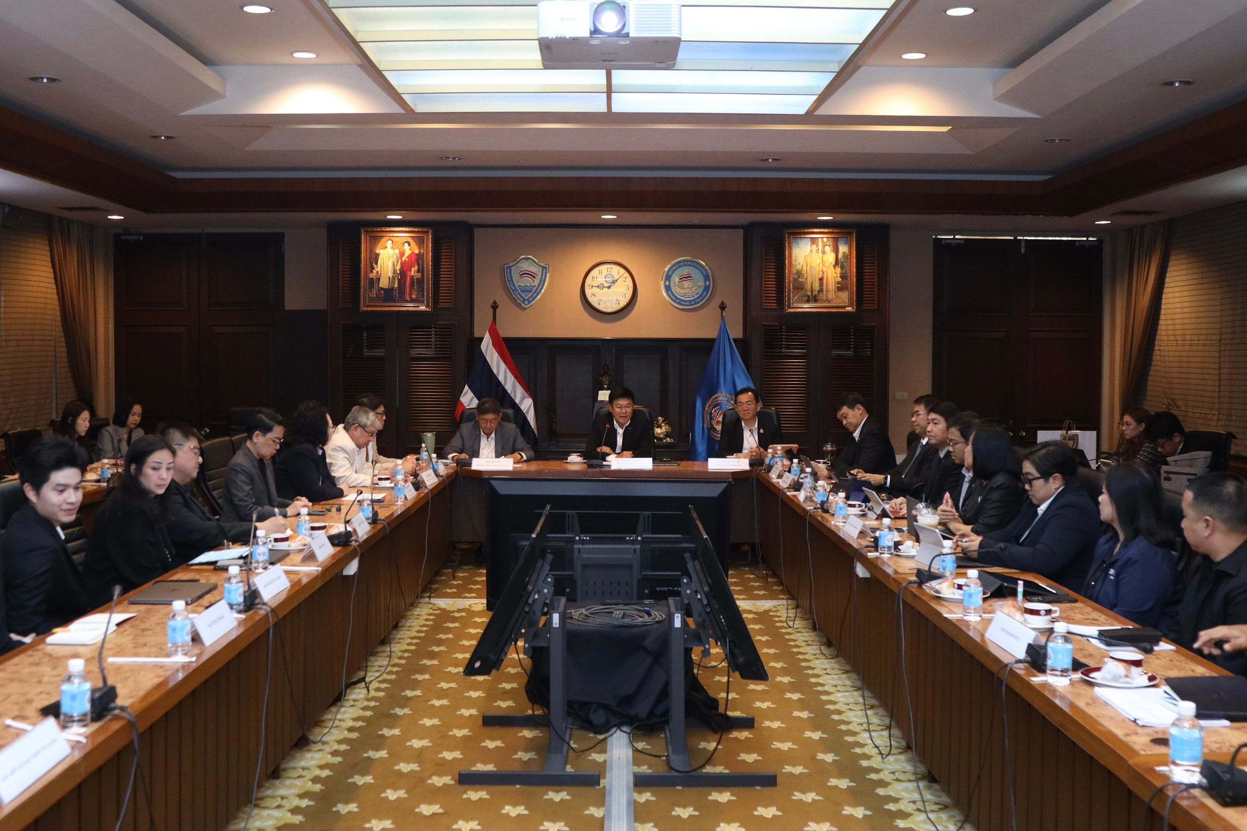 A formal meeting with many people seated around a long U-shaped conference table.