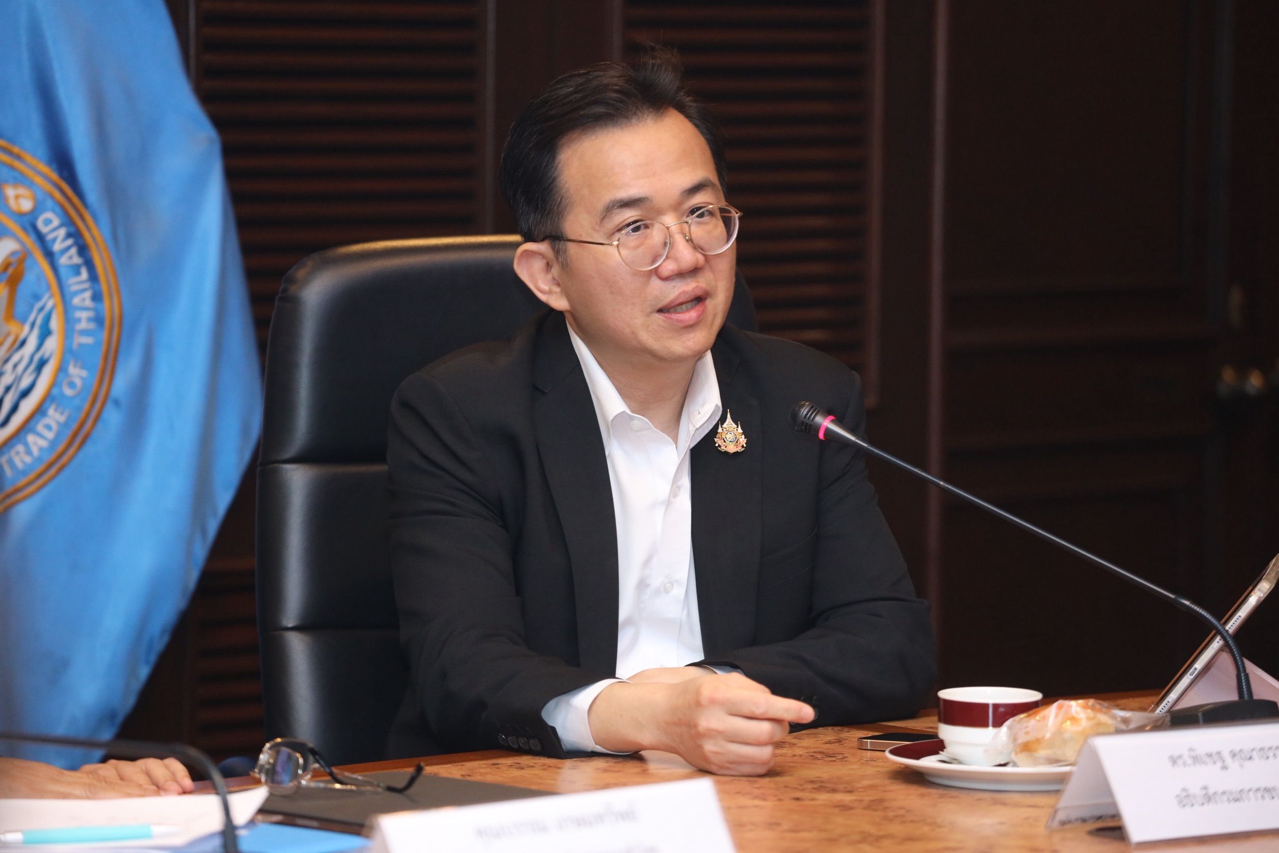 Man in suit and glasses speaks at a conference table with a microphone.