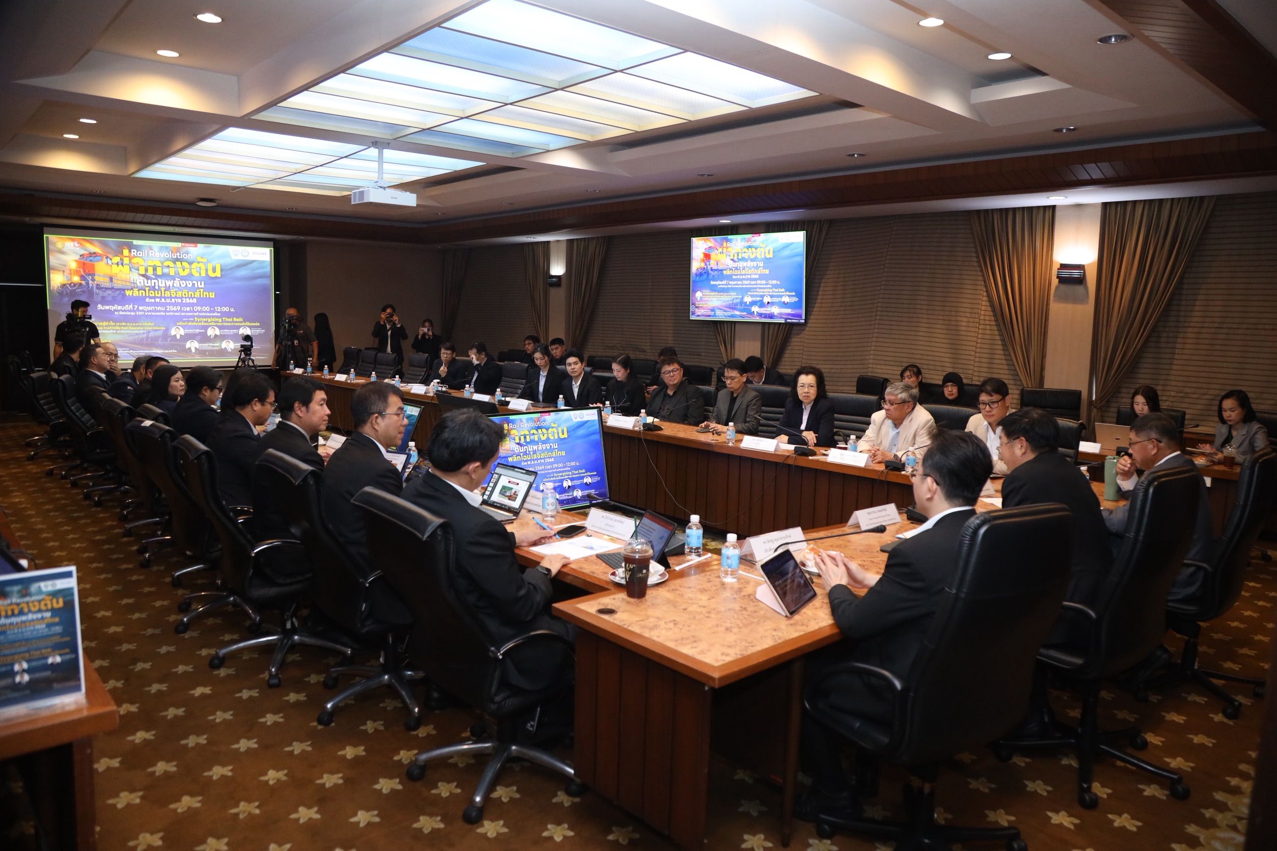 Professionals attend a serious business meeting in a large conference room with presentation screens.