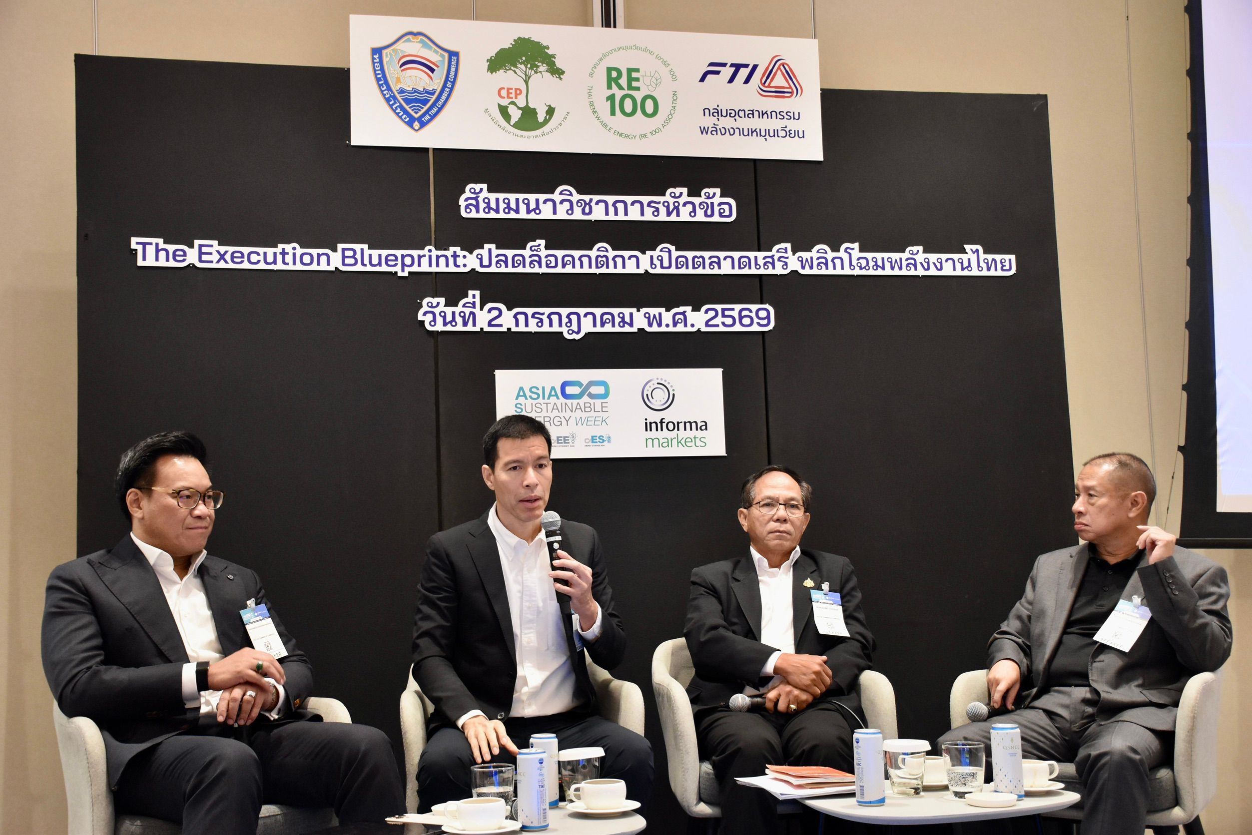 Four men sit on a stage, one speaking into a microphone at a decarbonization conference.