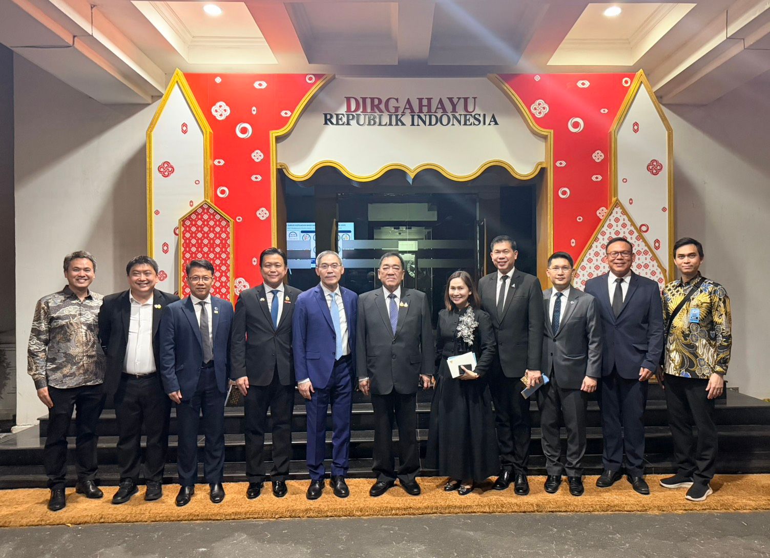 Thirteen people in formal wear pose before a decorative archway celebrating Indonesian Republic.