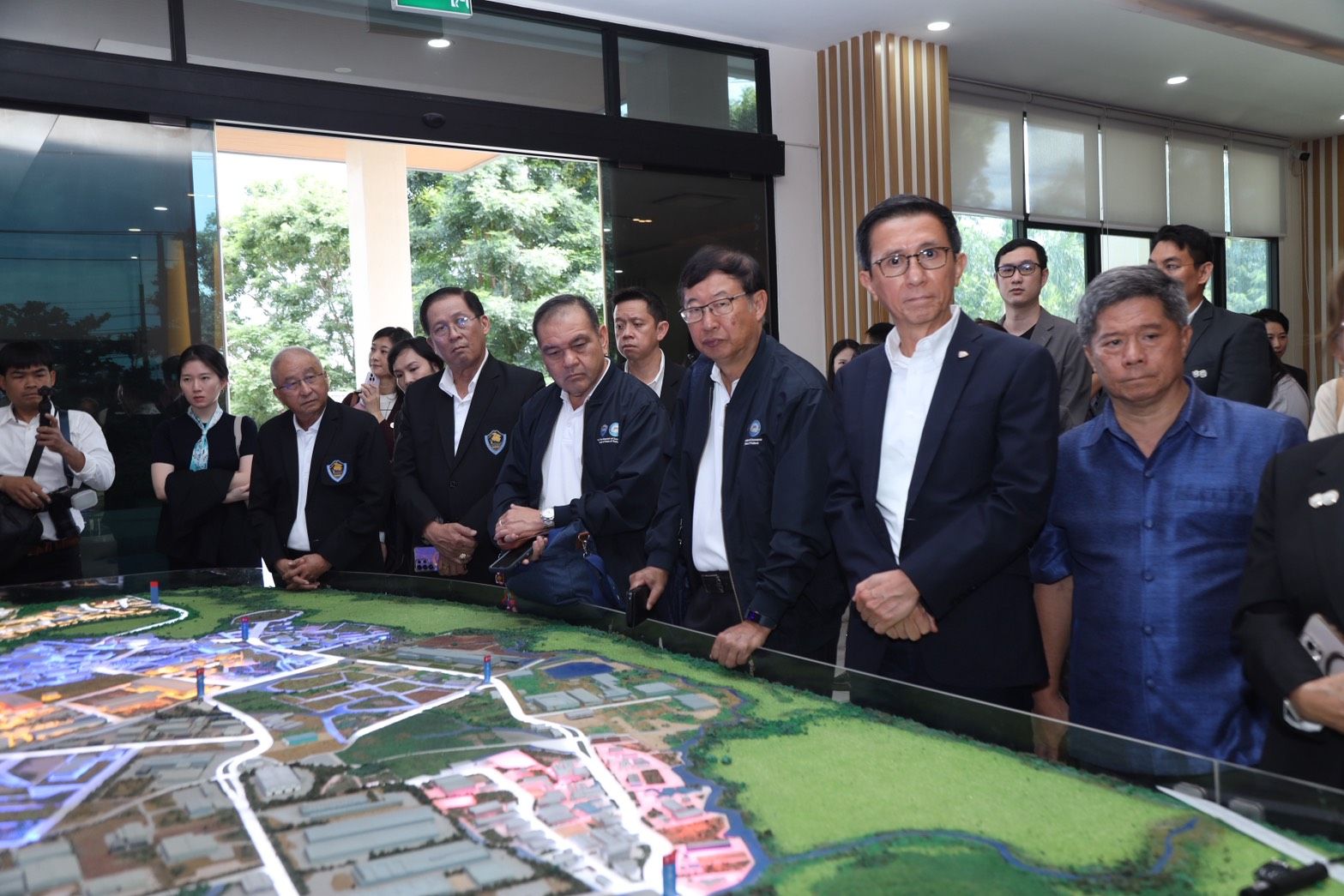 A group of officials intently observes a large scale model of a development plan.