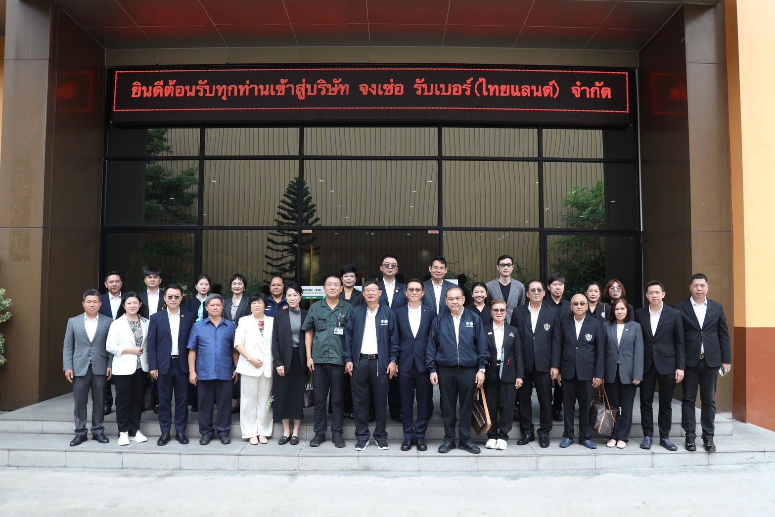 A large group of professionals poses in front of a modern building with a sign.