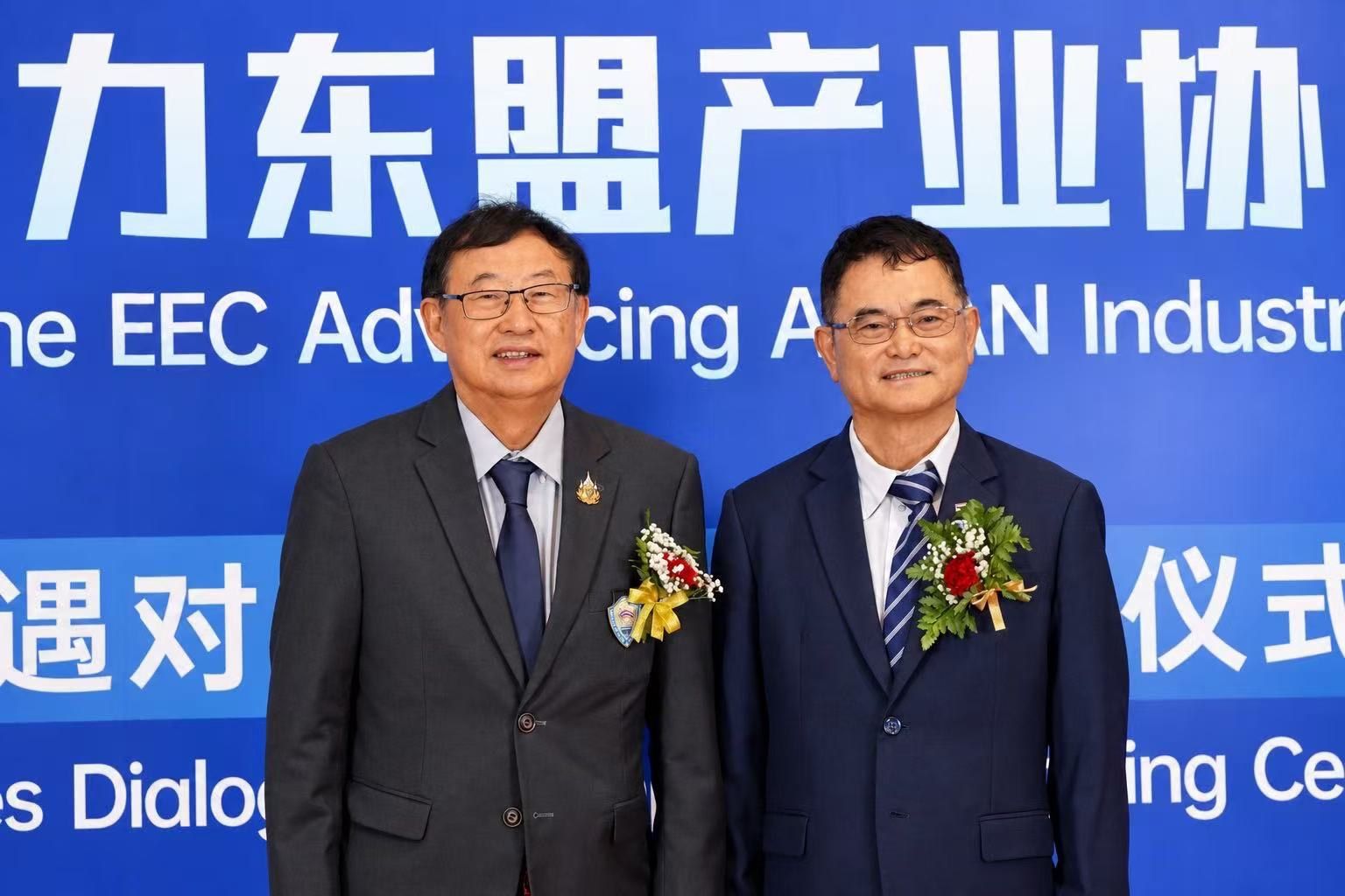 Two men in suits pose before a blue 'EEC Advancing ASEAN Industry' event backdrop.