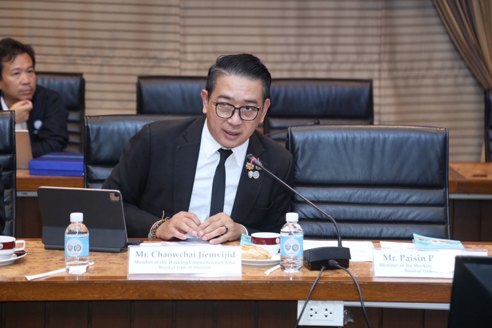 Mr. Chokchai Santisiri, a man in a suit and glasses, speaks at a formal meeting.